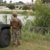 A National Guard soldier stands by a military vehicle in front of a barbed wire fence on the Rio Grande.