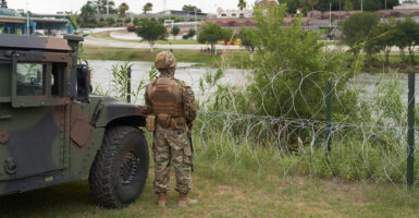 A National Guard soldier stands by a military vehicle in front of a barbed wire fence on the Rio Grande.