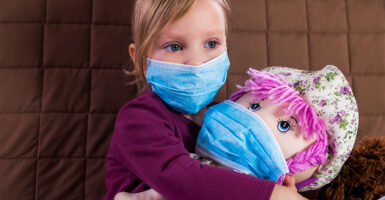 Girl in blue mask holds pink-haired doll.