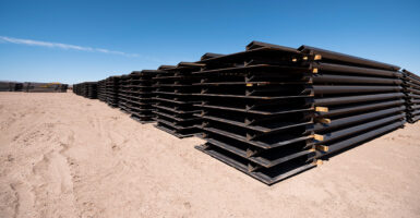 Stack of border wall panels lay in desert unused.