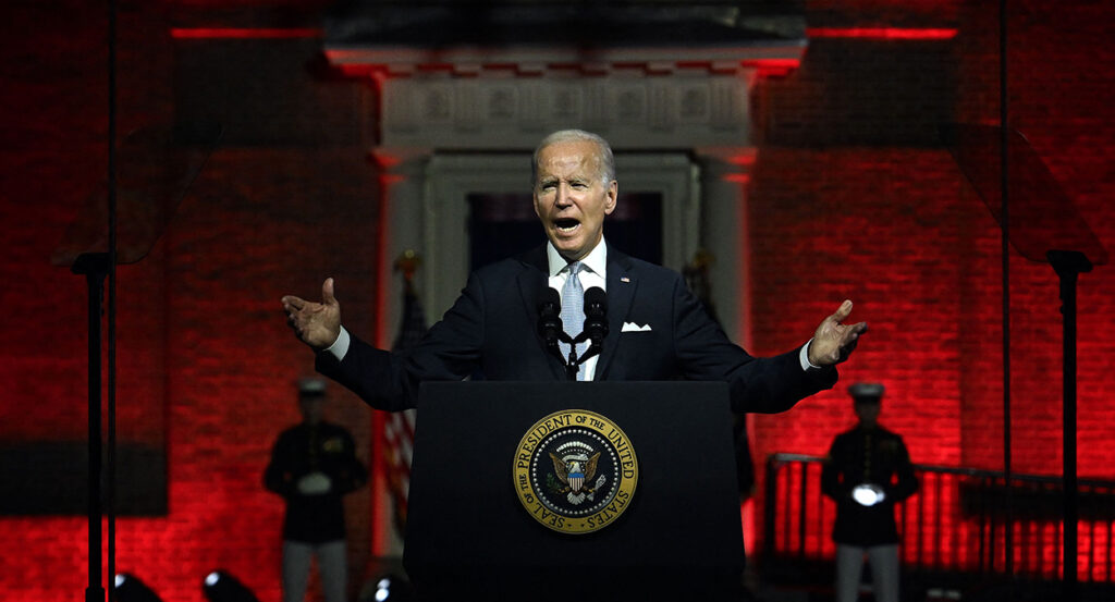 Joe Biden stands in a suit behind the presidential seal in front of a red backdrop in Philadelphia