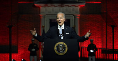 Joe Biden stands in a suit behind the presidential seal in front of a red backdrop in Philadelphia