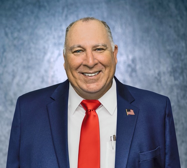 Michael Fesi in a blue suit with a red tie and an American flag