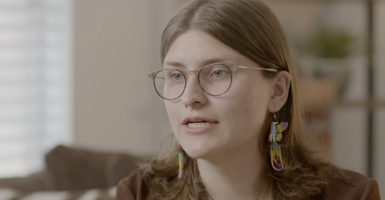 Woman with large glasses and prominent earrings speaks in video