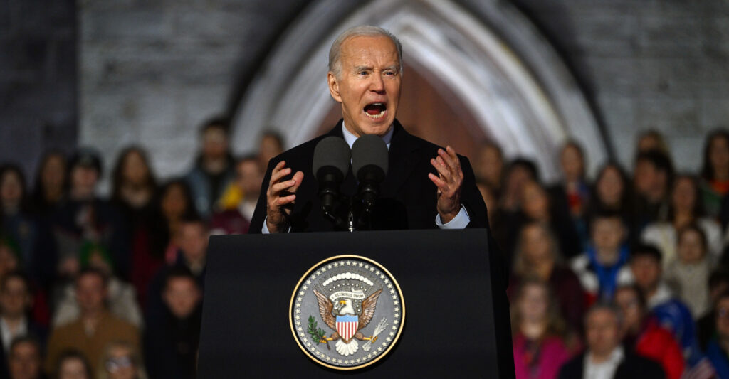 Joe Biden yells at a podium with the an American emblem on it in front of a crowd and church.