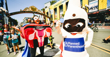 Two people dressed in character costumes of a vagina and a condom wearing Planned Parenthood signs in a parade.