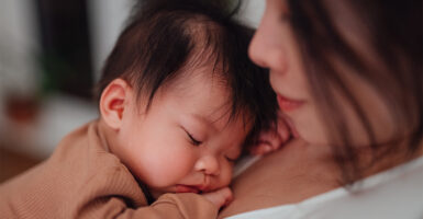 Young Asian mother holding sleeping baby.