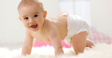 Baby on white rug wearing white diaper.
