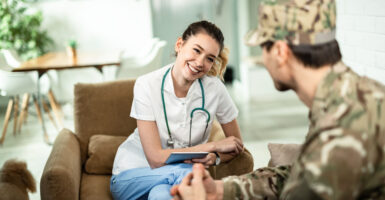 Happy nurse using touchpad and communicating with a soldier while visiting him at home.