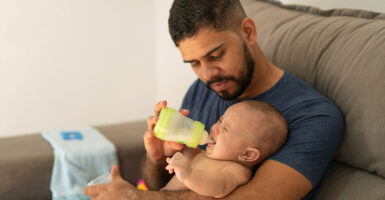 A man holds a baby and feeds it a bottle.