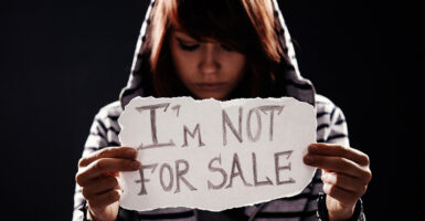 Brown-haired girl holds white sign that says "I'm not for sale."