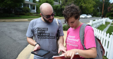 A man and woman look at a clipboard in a suburban neighborhood. They are outdoors wearing Planned Parenthood shirts.