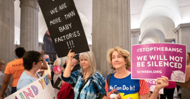 Two pro-abortion advocates hold signs in a political office building.