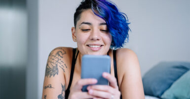 woman with short blue hair in bed using cell phone