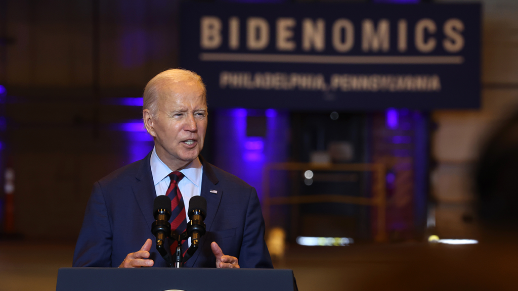 Joe Biden stands in front of a sign reading Bidenomics