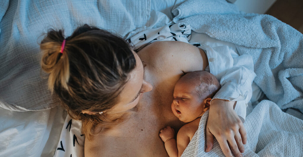 A mother holds her newborn baby in a hospital bed.