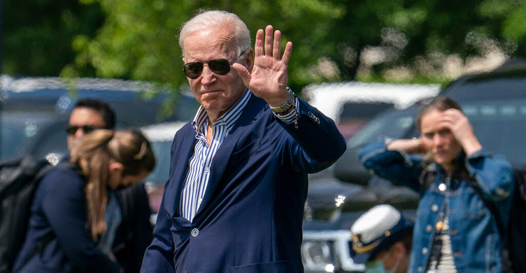 President Joe Biden wave as he prepares to board Marine One wearing sunglasses.