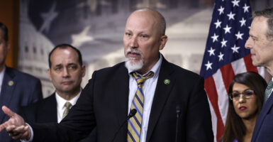 Chip Roy, bald and with a goatee, gestures in a black suit with a multi-colored striped tie
