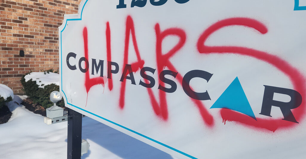 Red spray paint covers the CompassCare sign on a snowy March day.