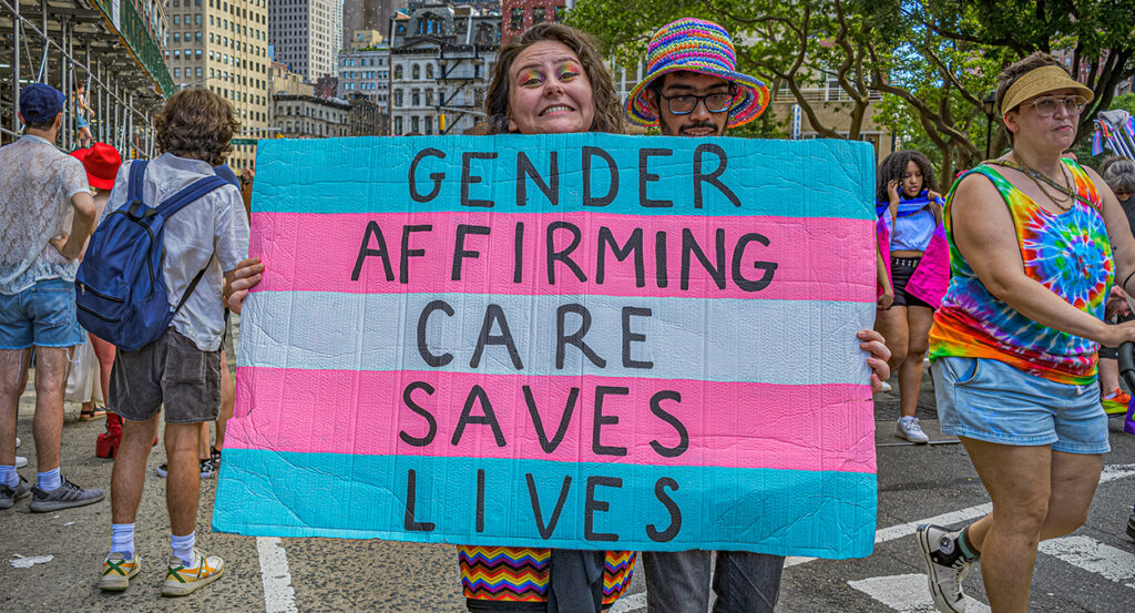 Woman holds transgender flag sign reading "gender-affirming care saves lives"