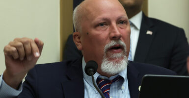 Rep. Chip Roy speaks into a microphone during a hearing wearing a dark suit and navy tie with white and red stripes.