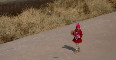 A young girl is seen walking holding a doll on the bank of the Rio Grande.