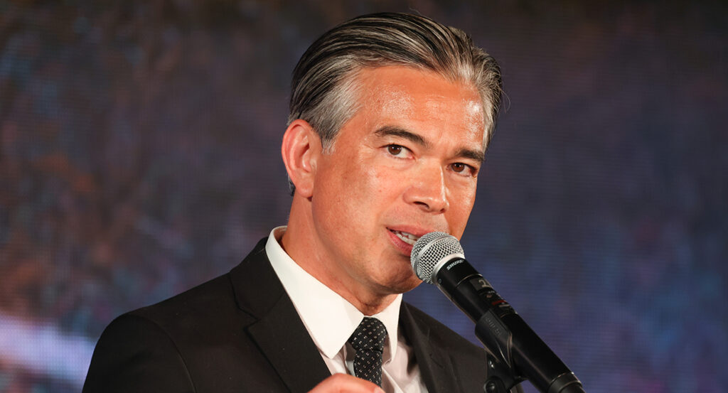 California Attorney General Rob Bonta in a black suit in front of a microphone