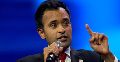 Vivek Ramaswamy raises a finger while speaking in the microphone and wearing a suit with an American flag pin.