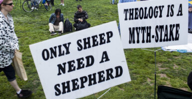 Two yard signs reading “Only Sheep Need a Shepherd” and “Theology Is a Myth-Stake”