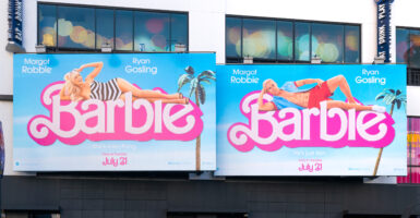 Two Barbie billboards next to each other, one with Barbie laying across the word 
