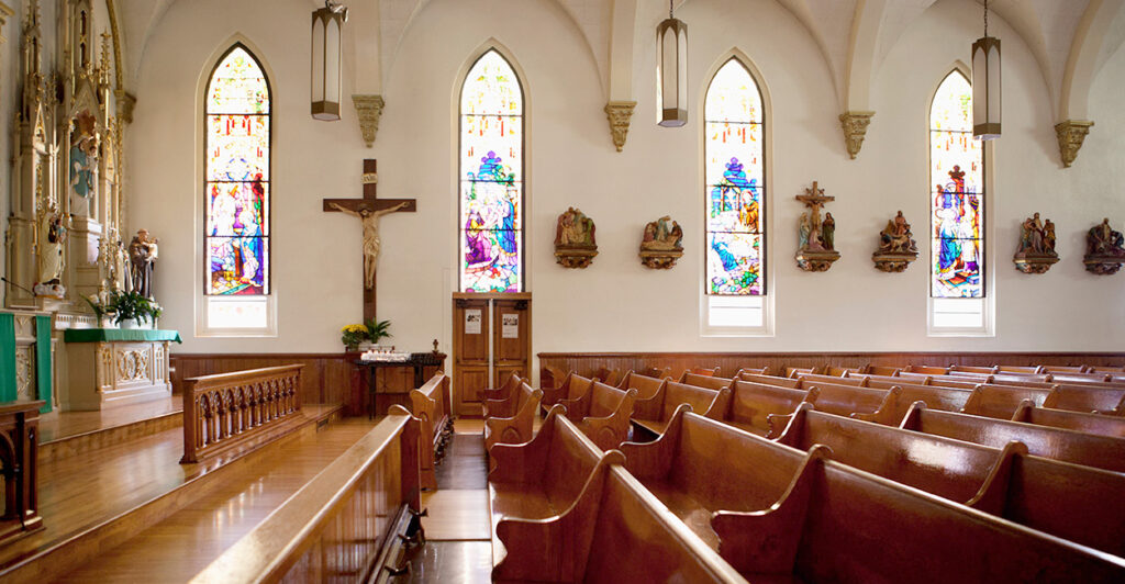 Light shines through stain glass windows onto church pews in a traditional church.