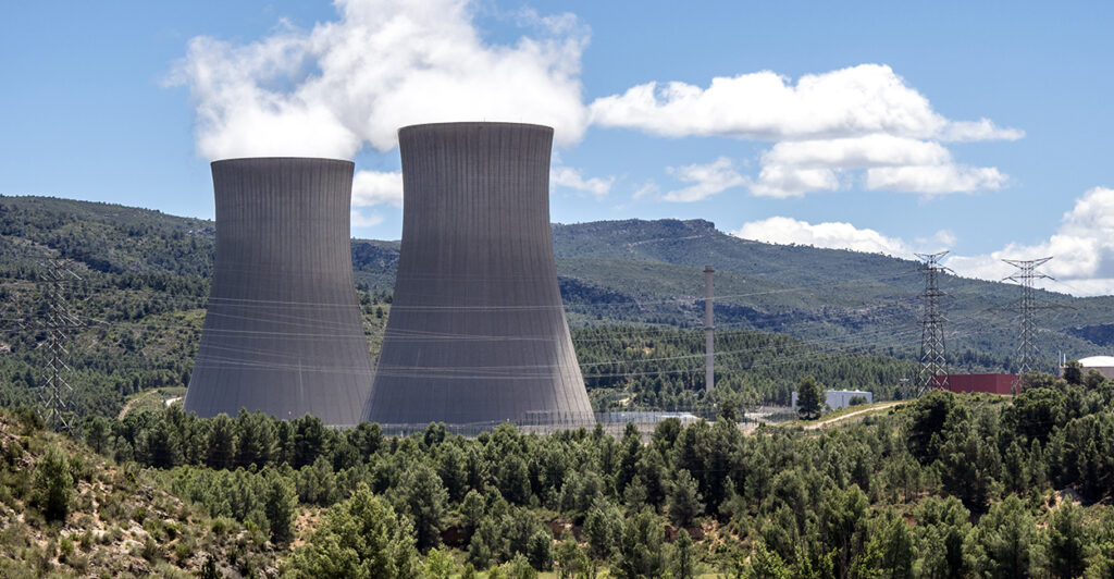Two nuclear power plant chimneys between mountains and forests.