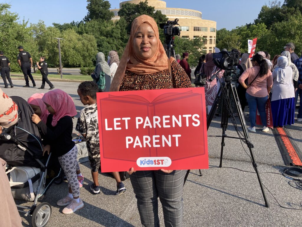 Black Muslim mom holds sign reading "Let Parents Parent"