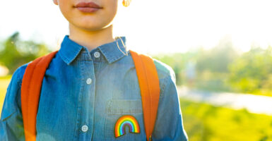 Young girl in denim T-shirt with rainbow Pride symbol and backpack outdoors