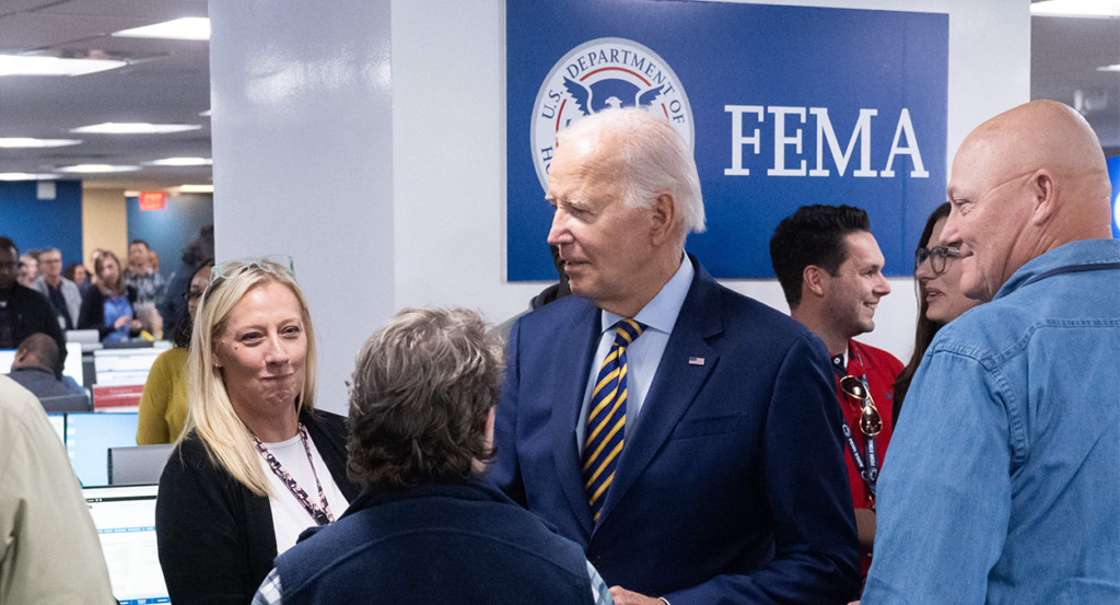 Joe Biden in a suit in front of the Federal Emergency Management Agency (FEMA) logo