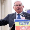 Robert Menendez in a pin-stripe suit speaks in front of a sign reading, "Student Debt Cancellation Is Legal"
