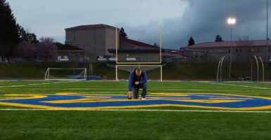Coach Kennedy take a knee in prayer at the Bremerton High School football field 50-yard line.