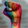 A fist painted in rainbow flag colors with a heart on the wrist