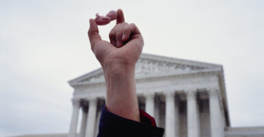 A hand raised in the air in front of the Supreme Court building holds a small plastic baby representing a child in the womb