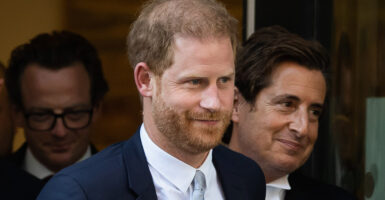 Prince Harry walks out of Rolls Building at the Royal Courts of Justice in London wearing a dark suit, white shirt, and silver tie.