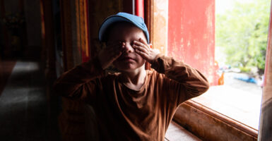 A little boy in a blue baseball hat covers his eyes.