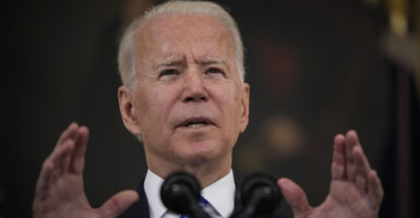 President Joe Biden gestures in front of a microphone while wearing a suit and a blue striped tie