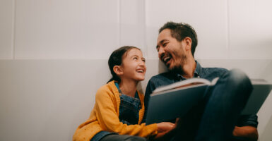 A father and daughter laugh together while reading a book.