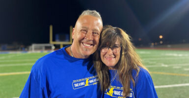 Coach Joe Kennedy and his wide Denise stand on the football field and smile.