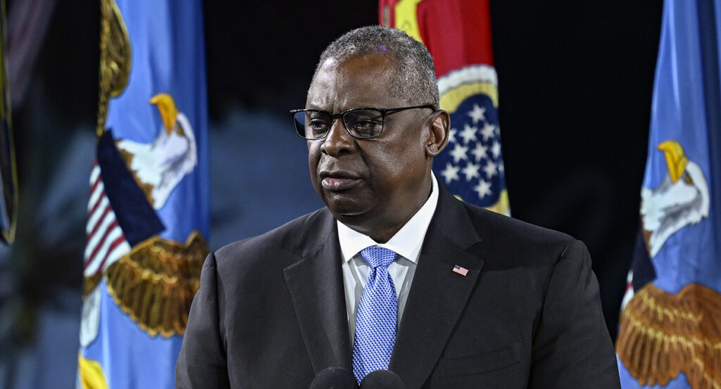 Secretary of Defense Lloyd Austin wearing a black suit and a black tie with an American flag pin.