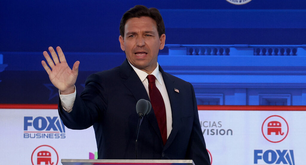 Ron DeSantis in a suit wearing an American flag pin waves during the Fox Business debate