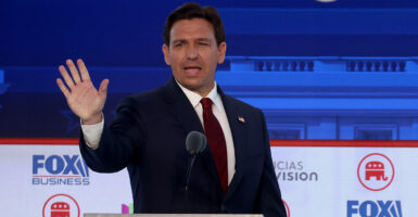 Ron DeSantis in a suit wearing an American flag pin waves during the Fox Business debate