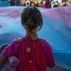A young girl holds the corner of a large transgender flag.