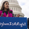 Rep. Alexandria Ocasio-Cortez speaks at a podium with a sign saying “Asylum is a right.”