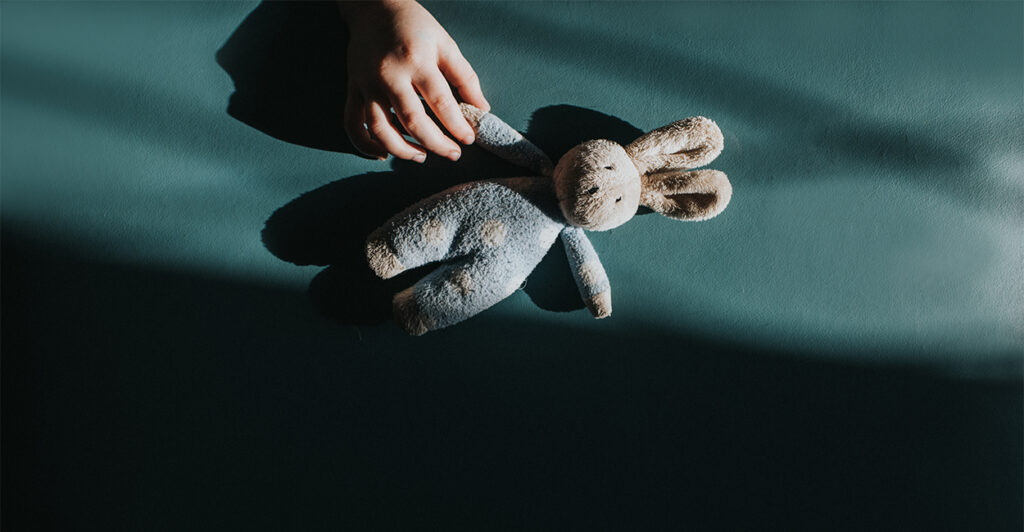 Lonely child's hand reaches for a small toy bunny